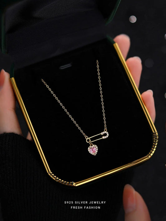 Necklace with a pink gemstone in a gold frame held by hands.