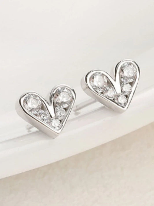 Heart-shaped silver earrings with clear gemstones on a light background