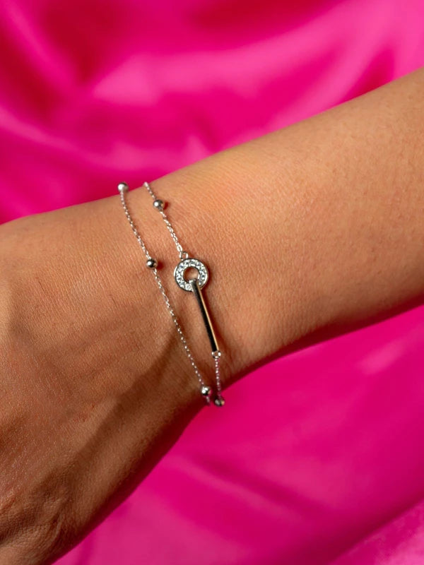 Silver key-shaped bracelet on a wrist against a pink background