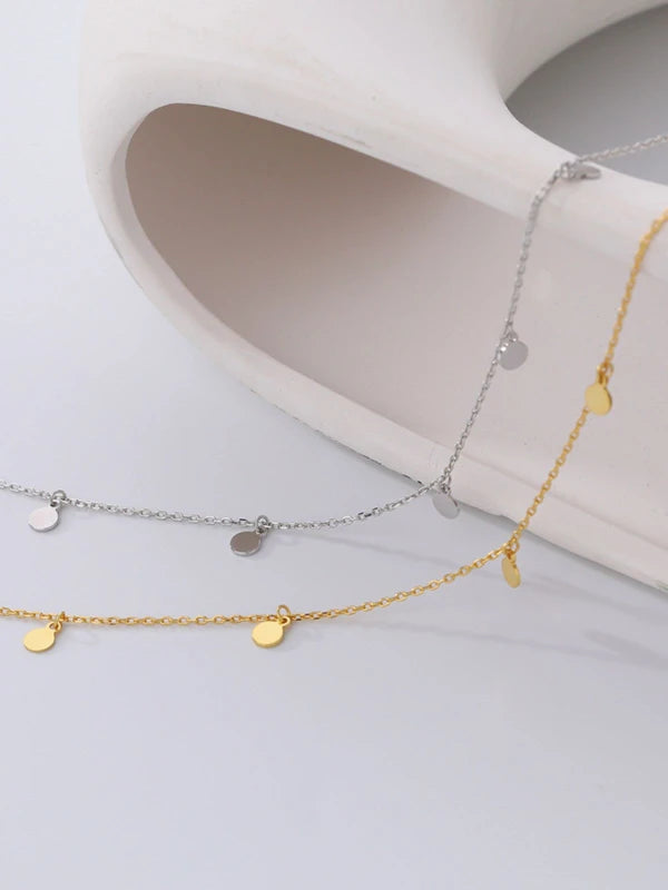 Two gold necklaces with small round pendants on a white surface.