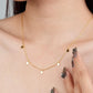 Gold necklace with small round pendants worn by a woman, with a hand touching the necklace.
