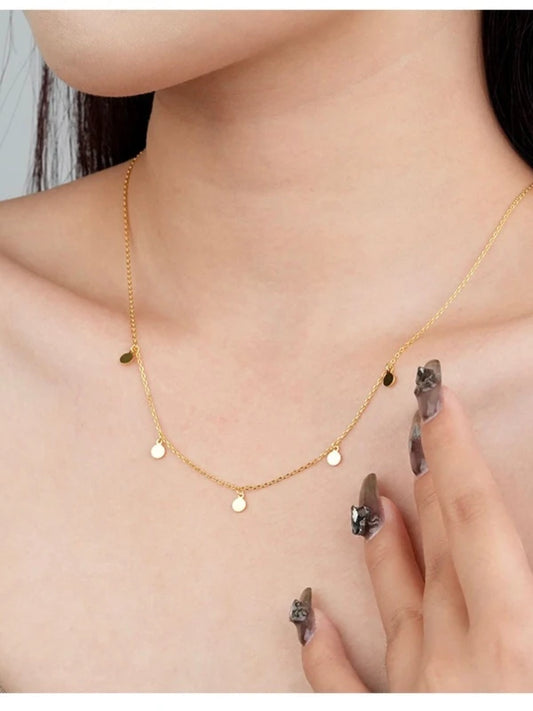Gold necklace with small round pendants worn by a woman, with a hand touching the necklace.