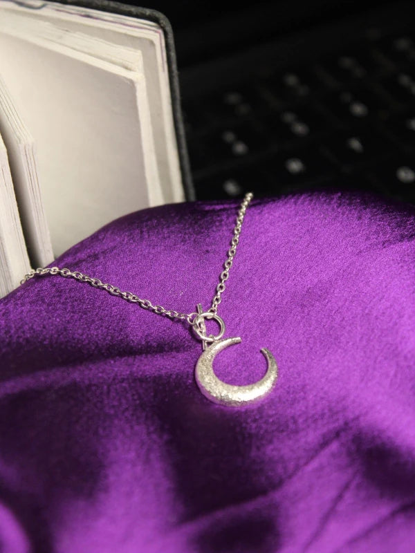 Silver crescent moon necklace on a purple fabric background