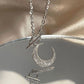 Silver necklace with a crescent moon pendant on a reflective surface.