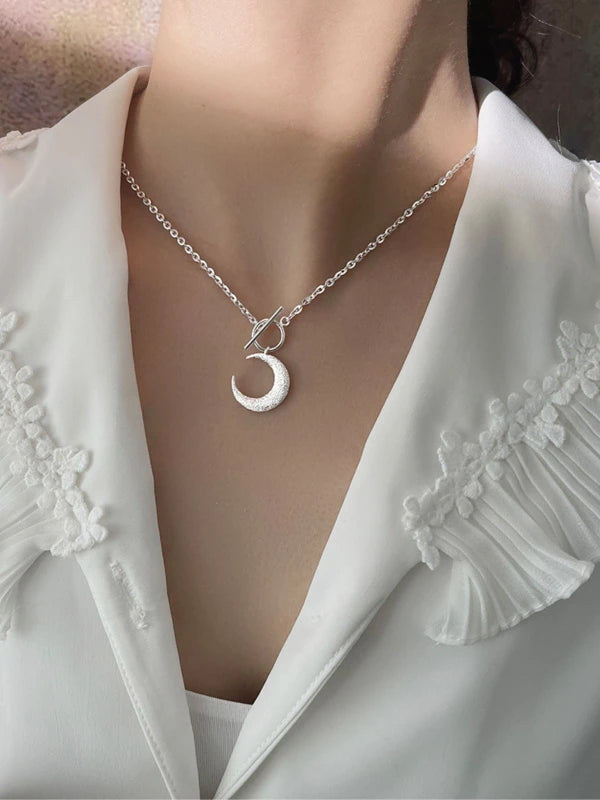 Silver necklace with a crescent moon pendant on a white blouse