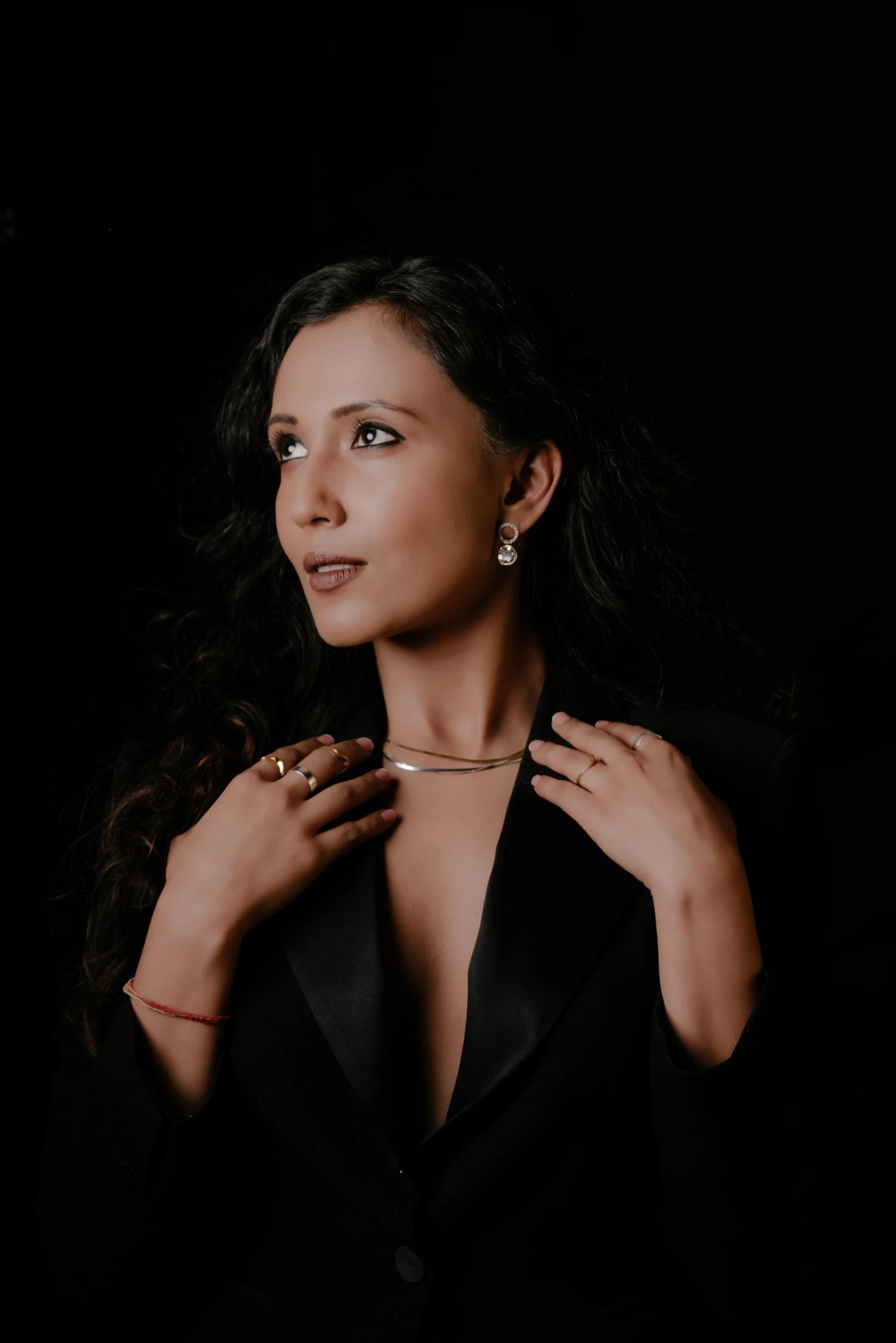 Woman wearing a black outfit with jewelry against a dark background