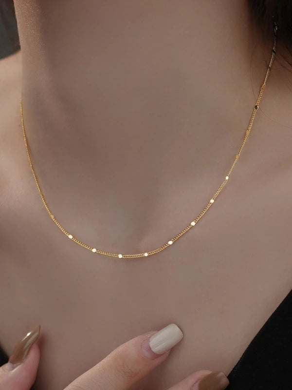 Gold necklace being worn on a woman's neck with a neutral background