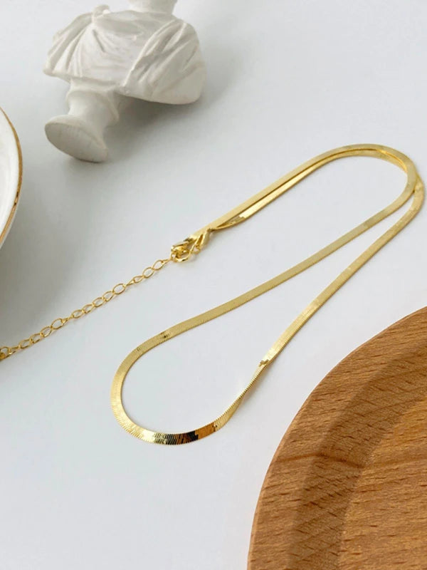 Gold necklace on a white surface with a wooden object in the background