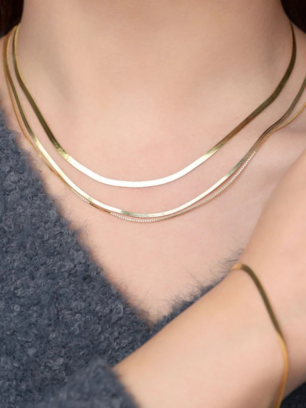 Two gold necklaces on a person wearing a dark blue sweater.