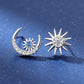Silver earrings shaped like a crescent moon and star with gemstones on a blue background