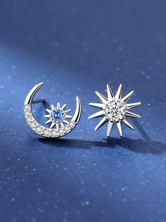 Silver earrings shaped like a crescent moon and star with gemstones on a blue background