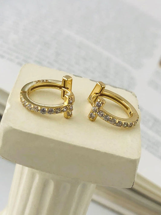 Gold hoop earrings with small stones on a white stand