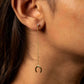 Close-up of an ear wearing a gold earring with a dangling crescent moon charm.