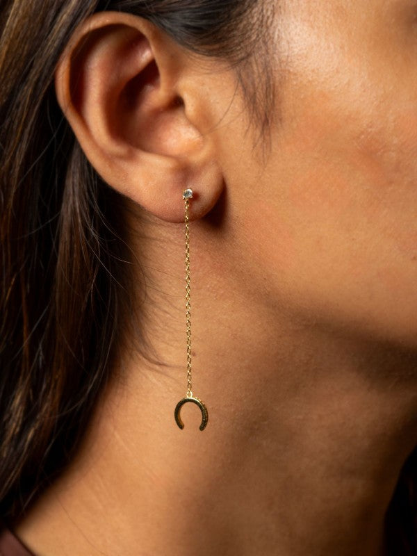 Close-up of an ear wearing a gold earring with a dangling crescent moon charm.