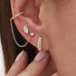 Close-up of an ear with gold earrings and a chain accessory.