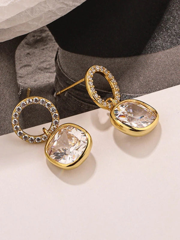 Gold earrings with clear gemstones on a neutral background