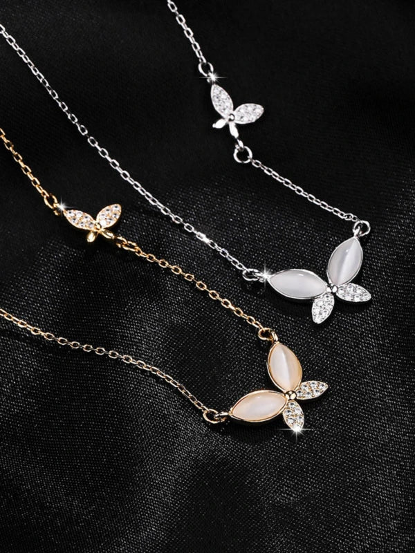 Three butterfly-shaped necklaces on a black fabric background
